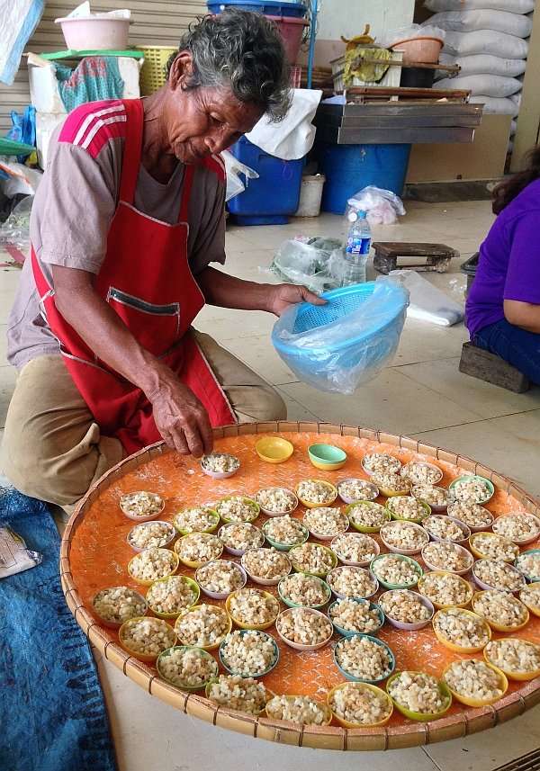 Ein älterer Herr verkauft Ameiseneier auf einem Markt in Zentralthailand. Er strahlt eine zufriedene Gelassenheit aus beim achtsamen Umgang mit seiner Ware.