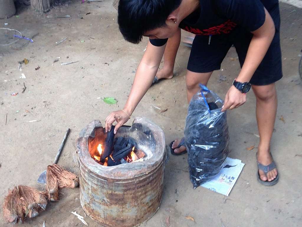 Dem Anfeuern der traditionellen Feuerstelle für Stockbrot mit Kokosfasern folgt konventionelle Holzkohle.